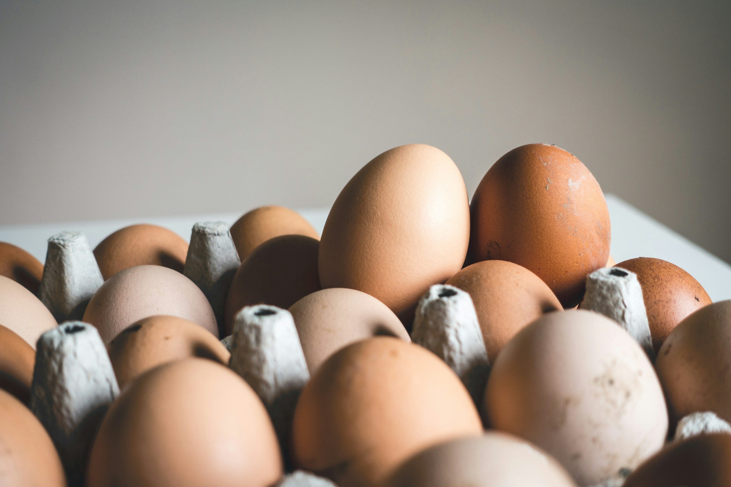 Close-up of various pasture-raised eggs in a carton, showcasing different shades of brown and beige, highlighting the natural colors and textures associated with high-quality eggs.