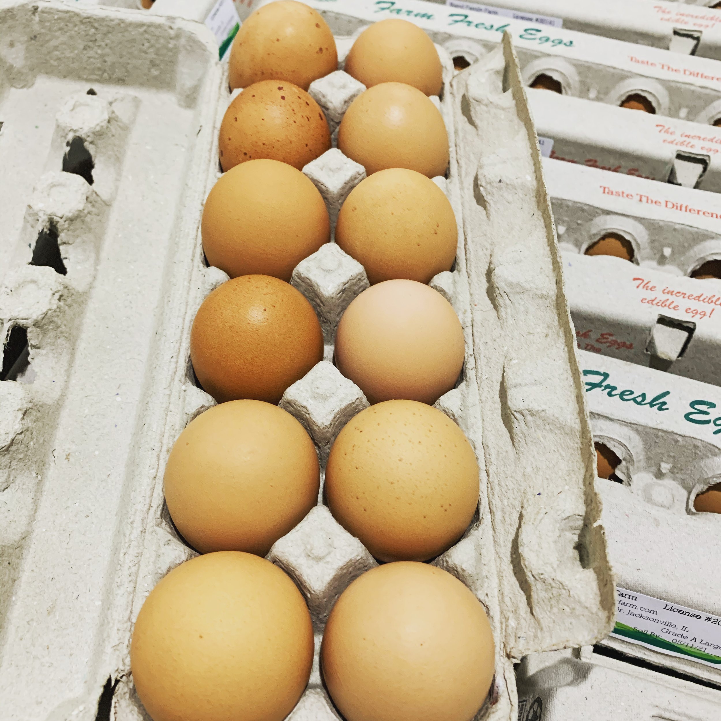 Bland+Family+Farm+Illinois+-+5CE70546-1D57-401E-AD19-4E0CFF1B0849 Fresh farm eggs in a carton, showcasing a variety of brown and beige eggs, with neatly packaged egg cartons in the background, highlighting farm-fresh quality.